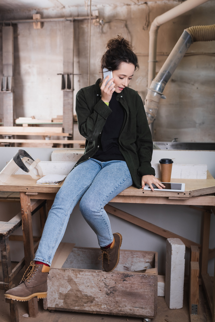 Travailleur du bois parlant sur smartphone près de tablette numérique et café en atelier  - Photo, image