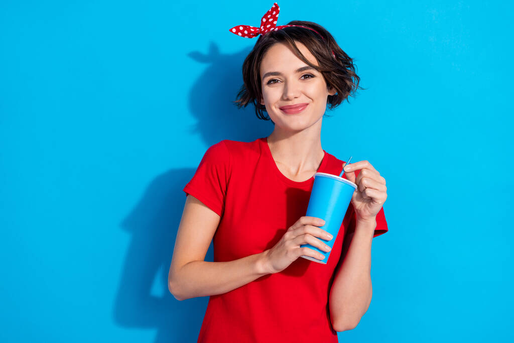 Foto di carino giovane bruna signora bere acqua indossare rosso t-shirt fascia isolata su sfondo di colore blu - Foto, immagini