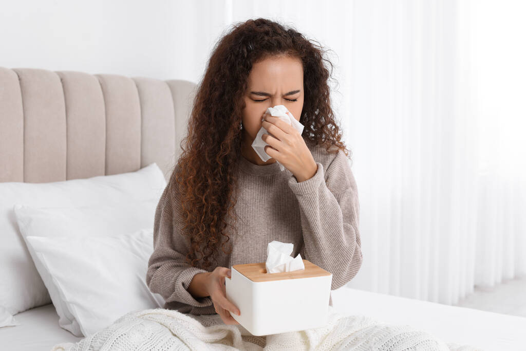 Sick African American woman with box of paper tissues suffering from cold in bed at home - Photo, Image