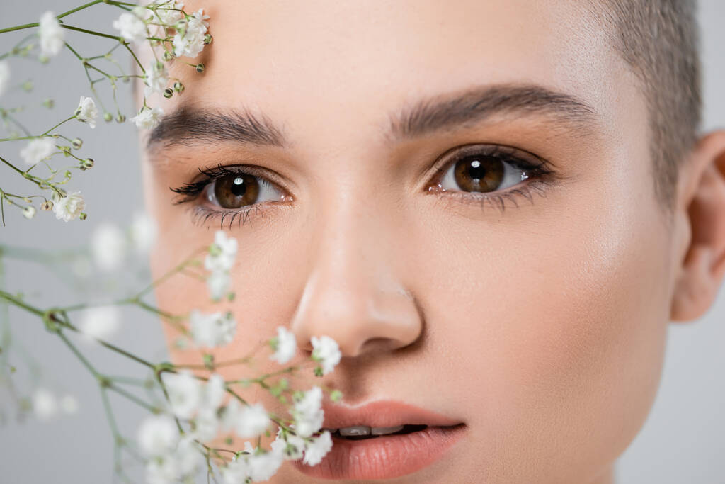 close up view of tiny gypsophila flowers near woman with natural makeup isolated on grey - Photo, Image