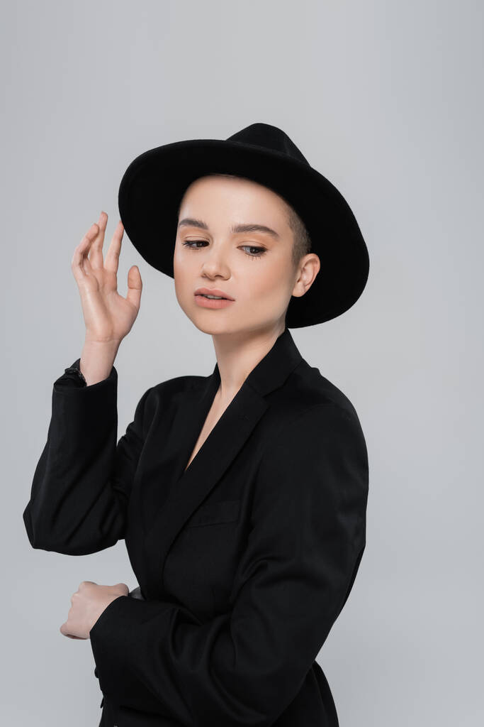 Nuori nainen musta bleiseri koskettaa lieri hattu eristetty harmaa - Valokuva, kuva