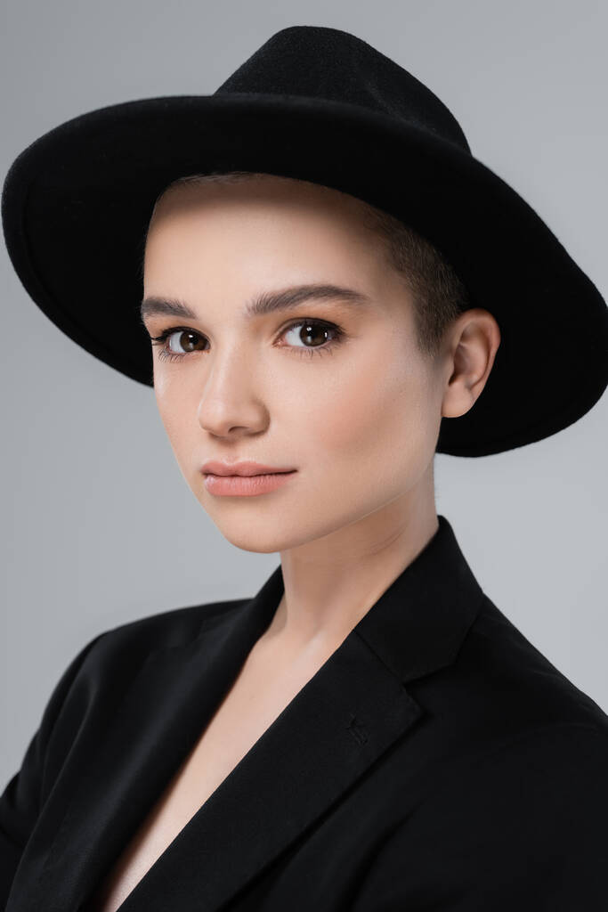 portré fiatal nő természetes smink, visel fekete karimás kalap, nézi kamera elszigetelt szürke - Fotó, kép
