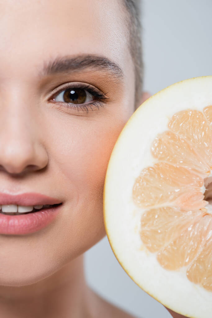 Nahaufnahme von Grapefruit halb in der Nähe abgeschnittenen weiblichen Gesicht isoliert auf grau - Foto, Bild