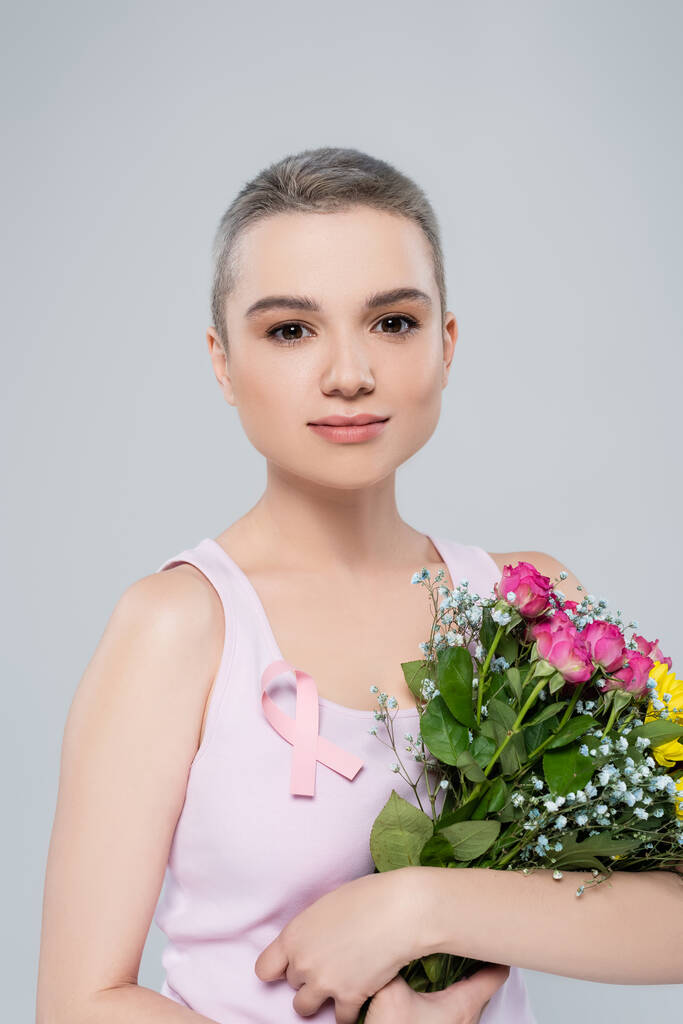 woman with breast awareness ribbon on tank top holding colorful bouquet isolated on grey - Photo, Image