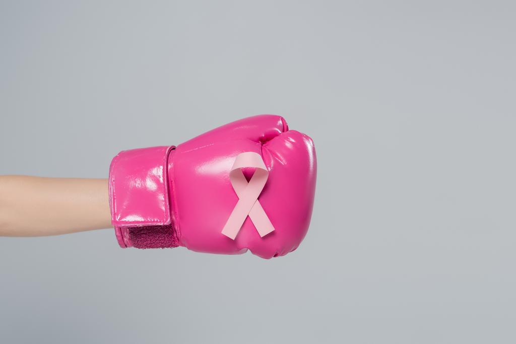 vista parcial de la mano femenina con cinta de sensibilización sobre el cáncer de mama en guante de boxeo rosa aislado en gris - Foto, imagen