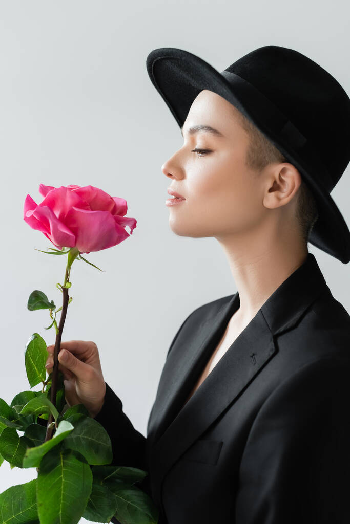 πλαϊνή όψη της trendy γυναίκα με φυσικό μακιγιάζ τρύπα ροζ τριαντάφυλλο απομονώνονται σε γκρι - Φωτογραφία, εικόνα