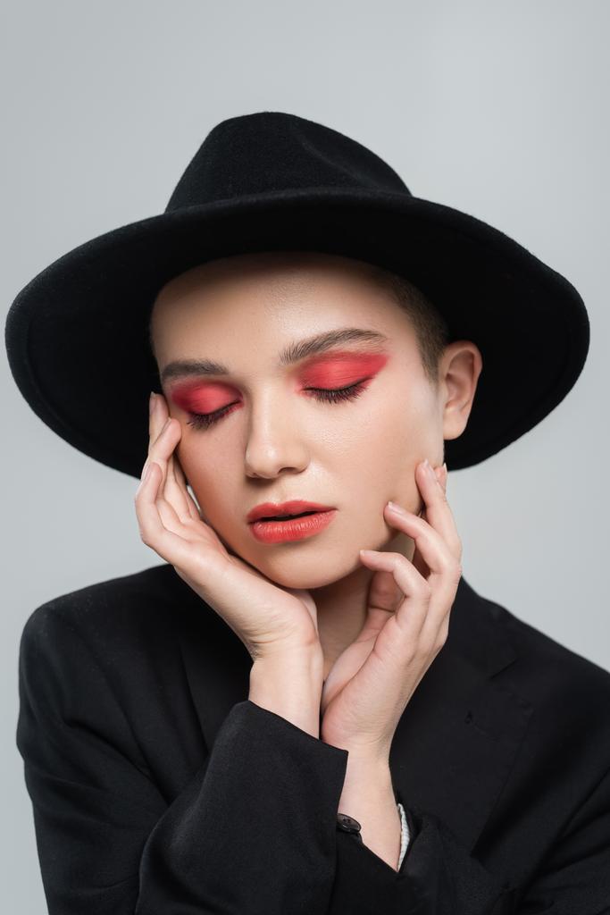 woman with closed eyes and carmine red makeup touching face isolated on grey - Photo, Image