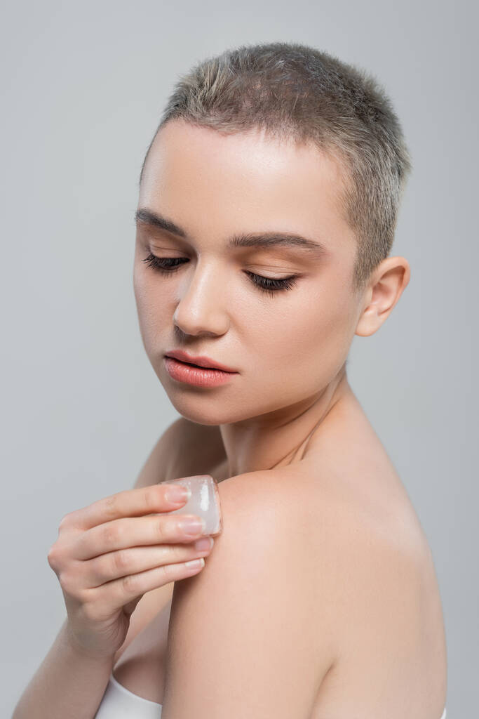 pretty woman with clean skin applying ice cube to naked shoulder isolated on grey - Photo, Image