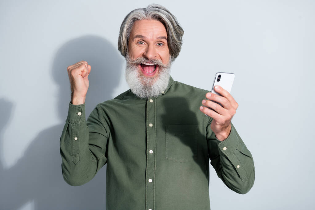 Portrét atraktivní veselý šedovlasý muž pomocí zařízení baví jako sledovat příspěvek smm izolované přes šedé pastelové barvy pozadí - Fotografie, Obrázek