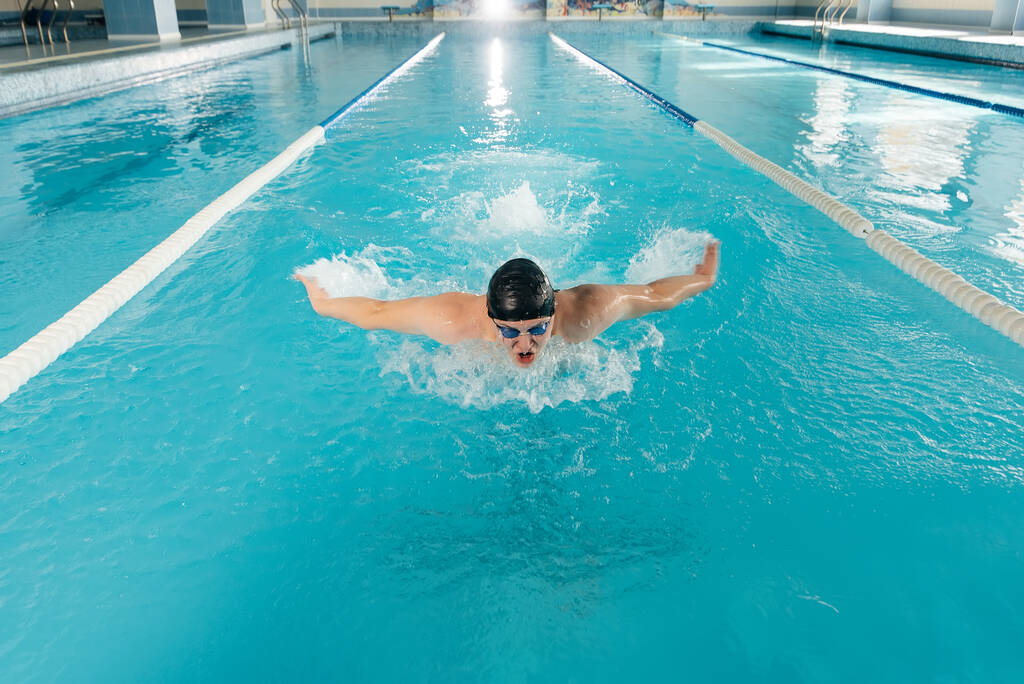 Een jongeman traint en zwemt in een modern zwembad. Sportontwikkeling. Voorbereiding op wedstrijden, en een gezonde levensstijl. Waterbehandelingen en een gezonde levensstijl. - Foto, afbeelding