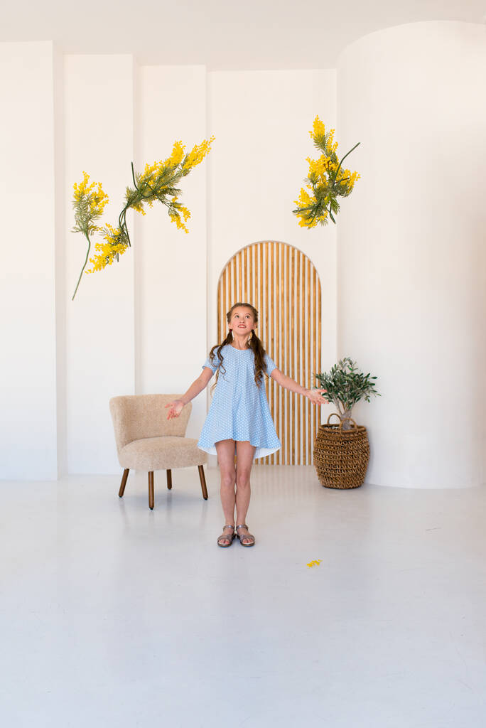 retrato de una niña con un ramo de flores de color amarillo primavera. Chica con un vestido azul. Interior de luz. - Foto, imagen