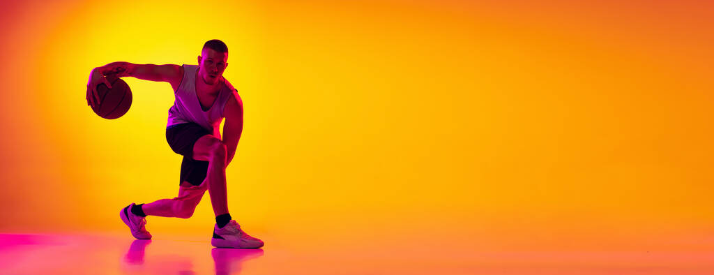 Flyer. Studioaufnahme eines muskulösen Mannes, Basketballspieler beim Training mit Ball isoliert auf gelb lila Hintergrund in Neonlicht. Schönheit, Sport, Bewegung, Aktivitätskonzepte. - Foto, Bild
