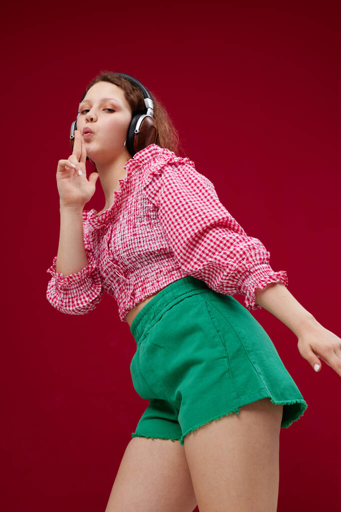 pretty woman in pink blouse and green shorts with headphones listening to music - Photo, Image