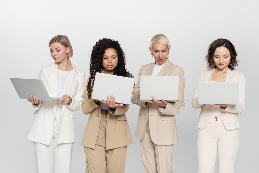 Multiethnische Geschäftsfrauen benutzen Laptops isoliert auf grauem Feminismus-Konzept - Foto, Bild
