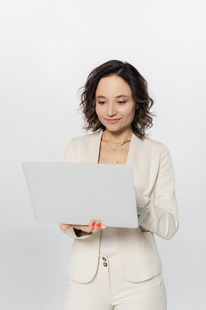 Businesswoman using laptop while standing isolated on grey  - Photo, Image