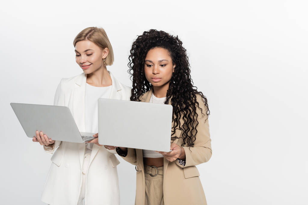 Young multiethnic businesswomen using laptops isolated on grey  - Photo, Image