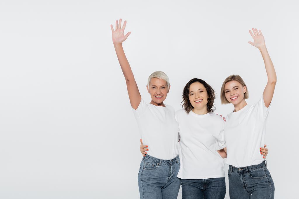 Glimlachende vrouwen in witte t-shirts zwaaiende handen geïsoleerd op grijs, feminisme concept - Foto, afbeelding
