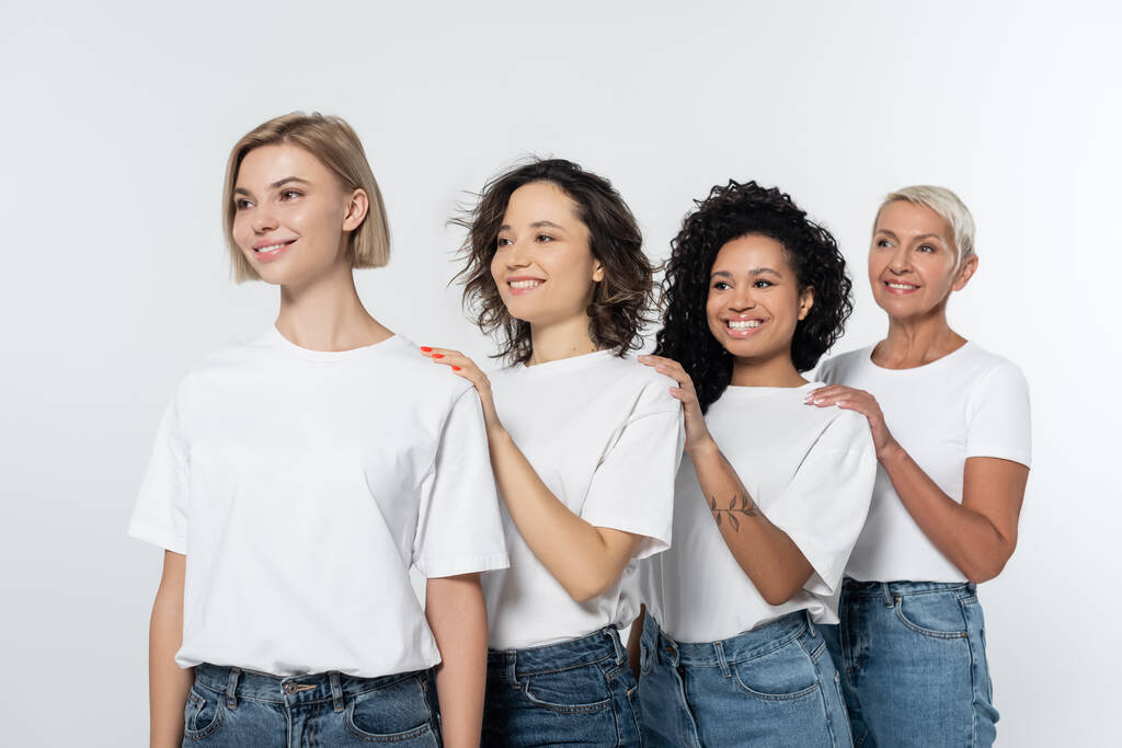 Usmívající se multietnické ženy v bílých tričkách odvracející pohled na šedé  - Fotografie, Obrázek