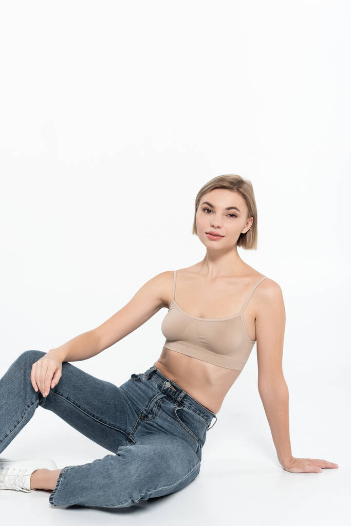Young blonde woman in jeans posing on grey background  - Photo, Image