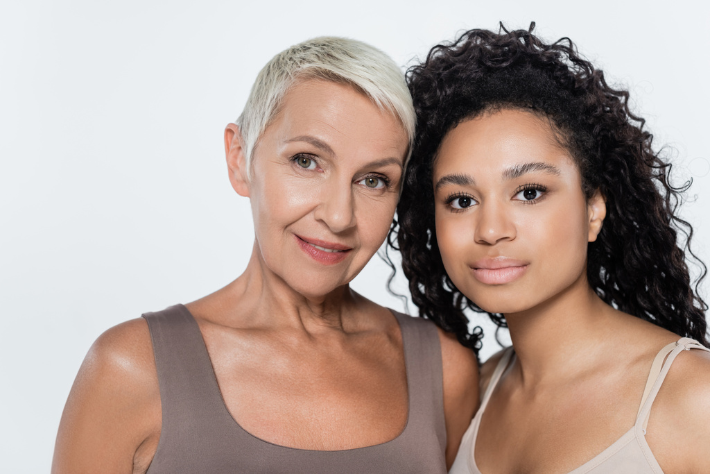 Curly african american woman looking at camera near grey haired friend isolated on grey  - Photo, Image