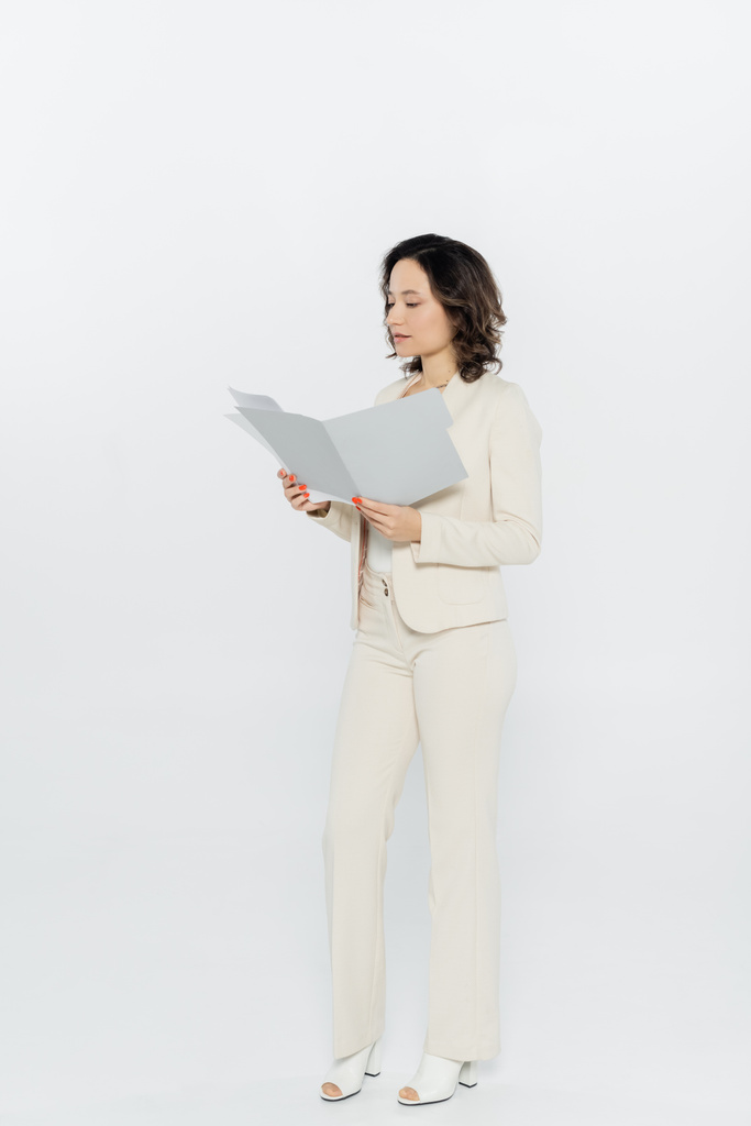 Volle Länge der brünetten Geschäftsfrau in formeller Kleidung hält Papiermappe auf grauem Hintergrund  - Foto, Bild
