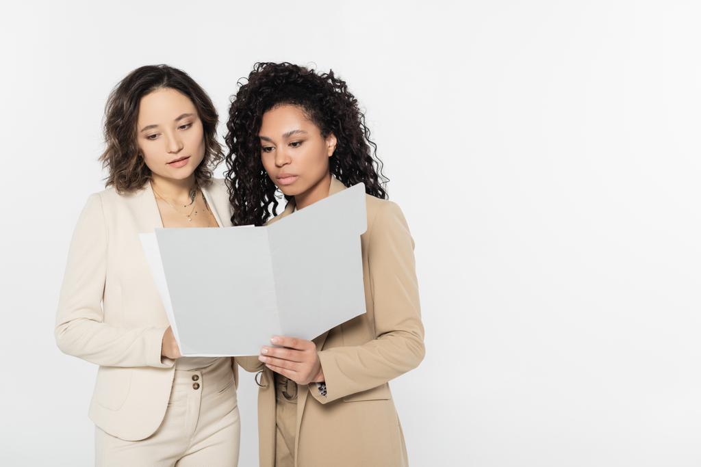 Empresarias multiétnicas mirando la carpeta de papel aislada en gris, concepto feminista - Foto, Imagen