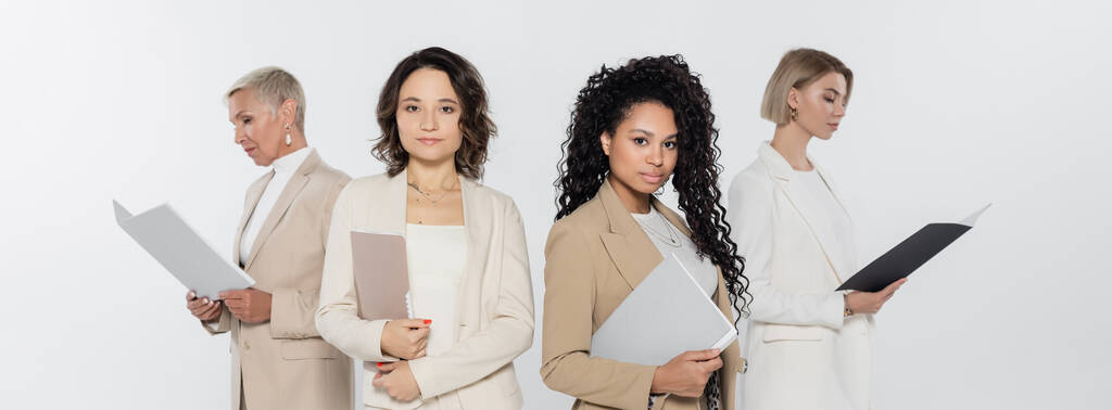Мультиэтнические предпринимательницы держат бумажные папки рядом с коллегами изолированными на сером, баннере  - Фото, изображение
