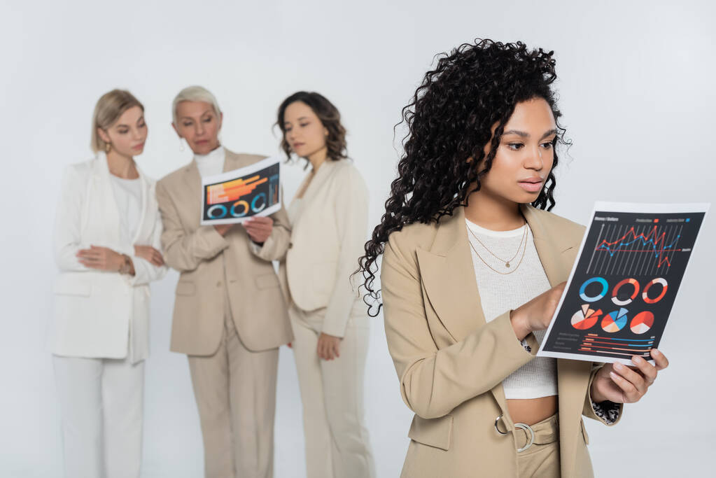 Femme d'affaires afro-américaine tenant un document près de collègues flous isolés sur gris  - Photo, image