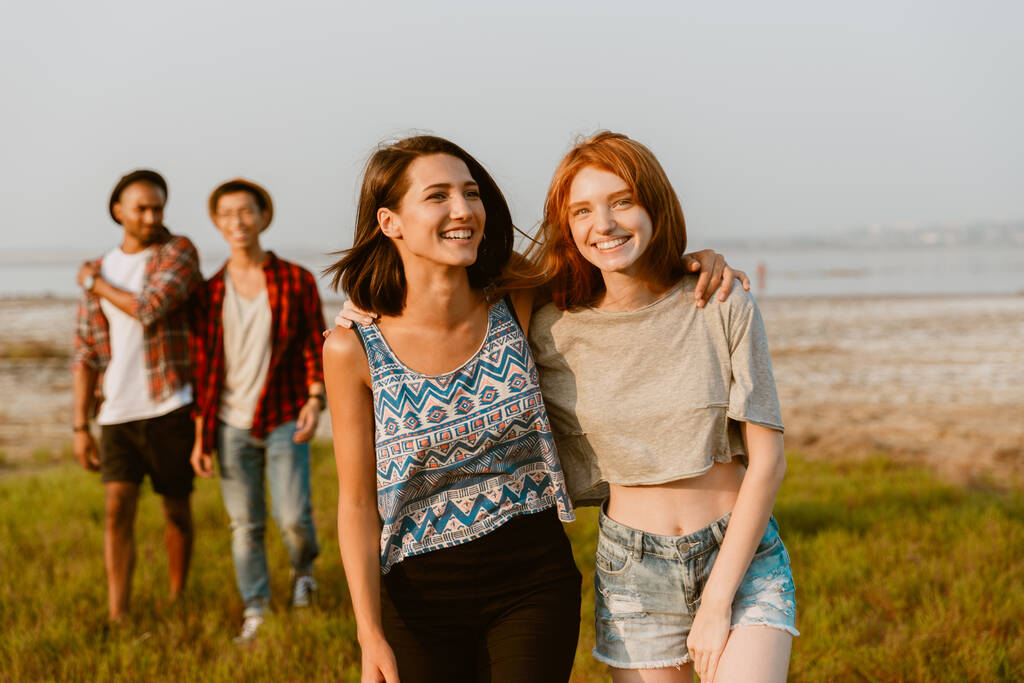 Jovens amigos multirraciais abraçando e sorrindo juntos enquanto caminham ao ar livre - Foto, Imagem
