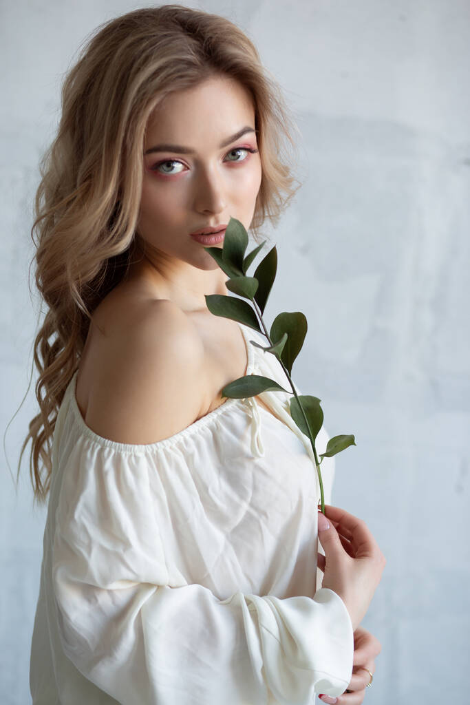 Portret seksownej uroczej kobiety w białej bluzce z kwiatem w rękach. Studio zdjęcie na szarym tle - Zdjęcie, obraz