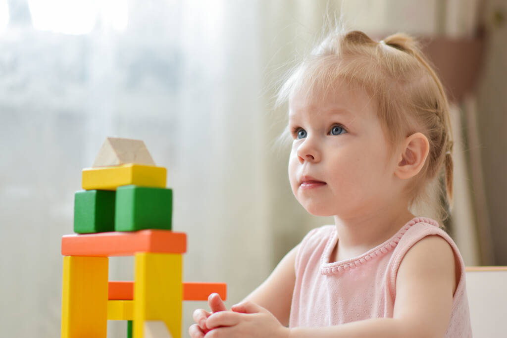 Un bambino piccolo sta giocando a un tavolo con un kit di costruzione in legno. Un gioco con i cubi. Giochi per bambini - Foto, immagini