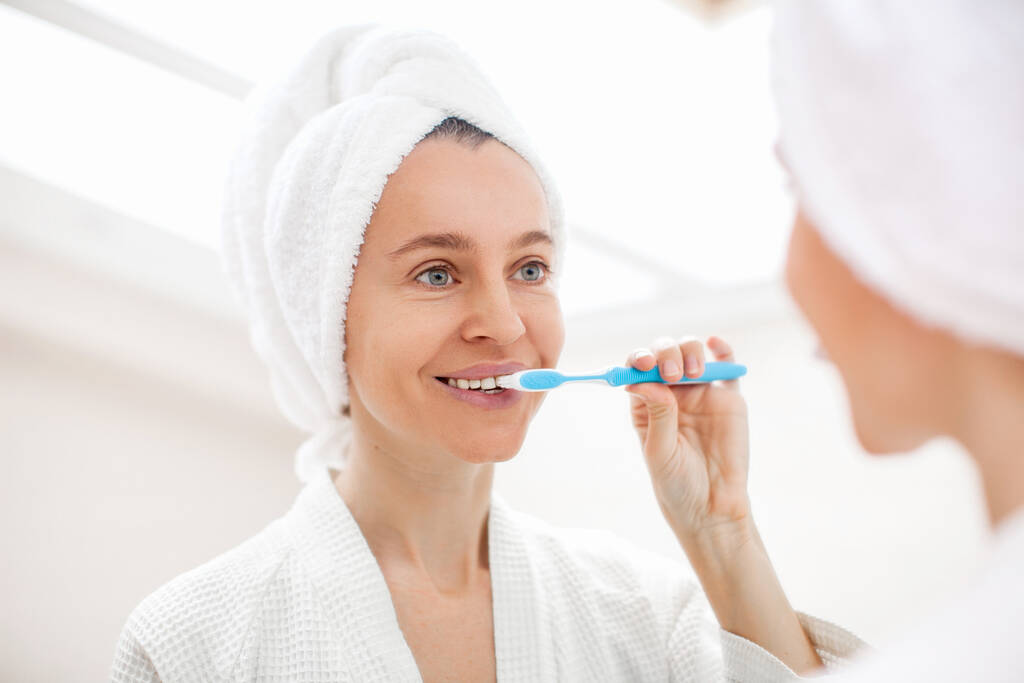 Happy Lady szczotkowanie zębów ze szczoteczką do zębów w średnim wieku kobieta stoi w łazience w środku rano - Zdjęcie, obraz