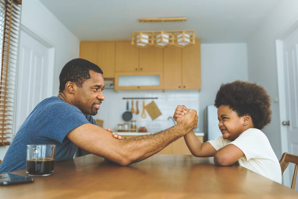 Чорно-африканський батько змагається в армрестлінгу зі своїм маленьким хлопчиком на кухні вдома. - Фото, зображення
