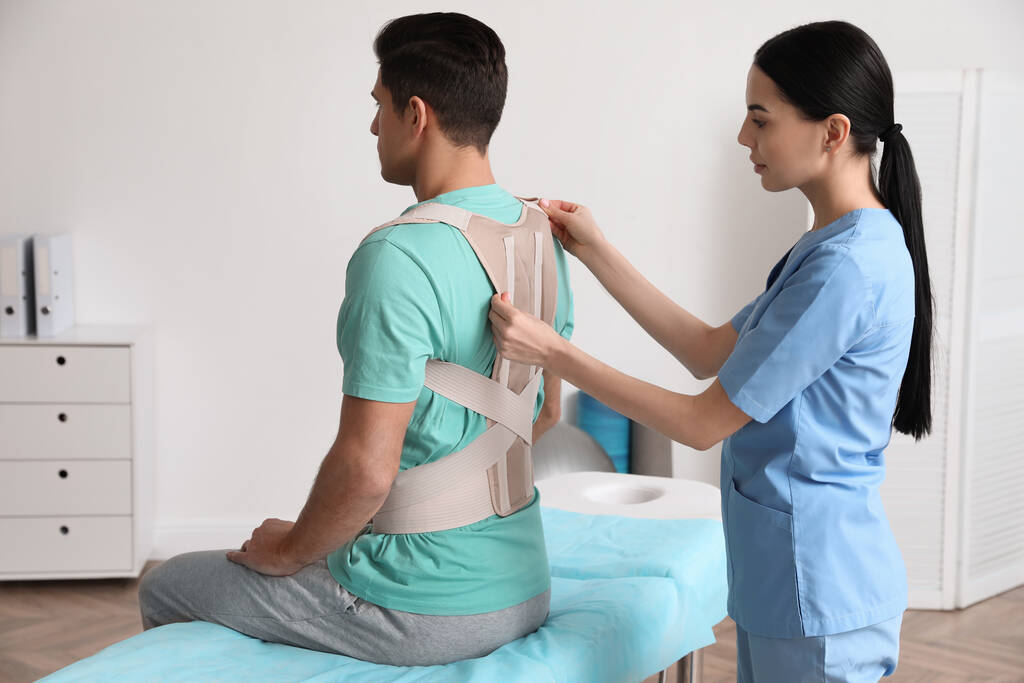 Orthopédiste aidant le patient à mettre sur correcteur de posture à la clinique. Traitement de la scoliose - Photo, image