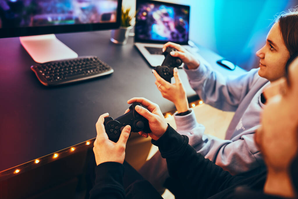 Freunde beim Videospiel zu Hause. Gamer mit Gamepads sitzen vor dem Bildschirm. Luftschlangen Mädchen und Jungen spielen online in dunklen Raum beleuchtet von Neonlichtern. Wettbewerb und Spaß - Foto, Bild