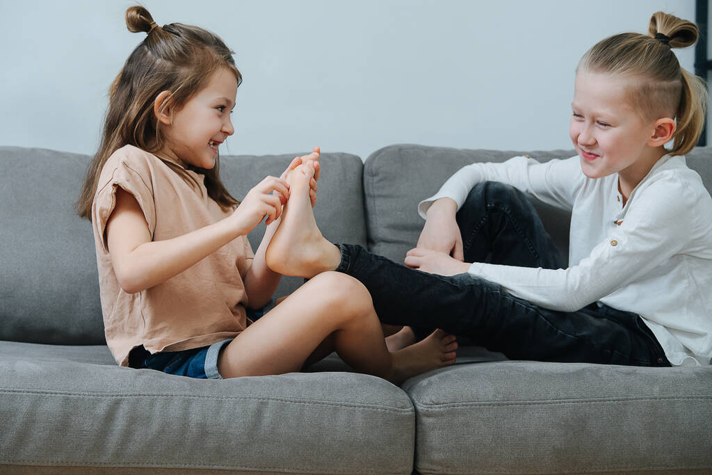 Chica traviesa tratando de hacerle cosquillas al pie del chico, ambos se ríen. En la vista lateral del sofá. - Foto, imagen