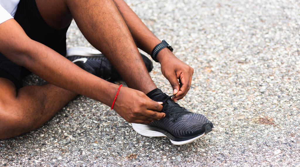Κοντινό πλάνο Ασιάτης δρομέας μαύρος άνδρας κάθεται κορδόνι προσπαθεί να τρέξει παπούτσια ετοιμάζεται για τρέξιμο και να τρέξει στο υπαίθριο δρόμο, την υγεία άσκηση έννοια προπόνηση - Φωτογραφία, εικόνα