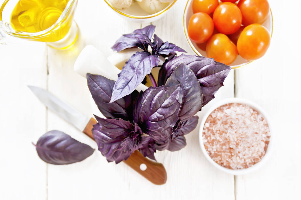 Świeża fioletowa bazylia w zaprawie, różowa sól, pomidory i champignons w misach, olej roślinny w sosie i nóż na drewnianym tle deski z góry - Zdjęcie, obraz