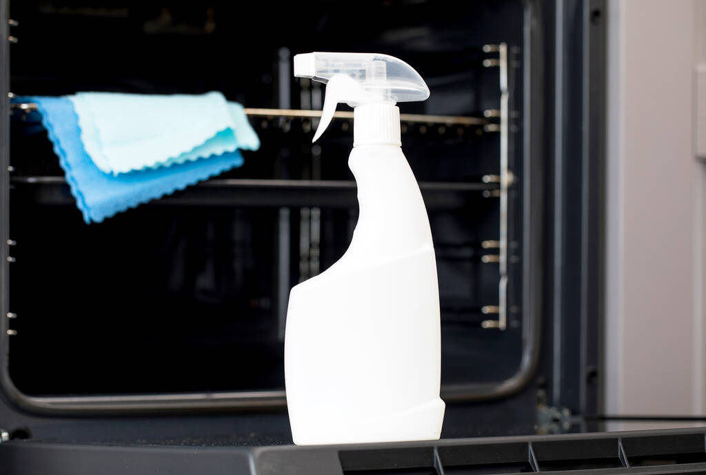 Na porta de um forno aberto há um mock-up de um frasco de spray branco com detergente do forno. Limpeza geral da cozinha. - Foto, Imagem