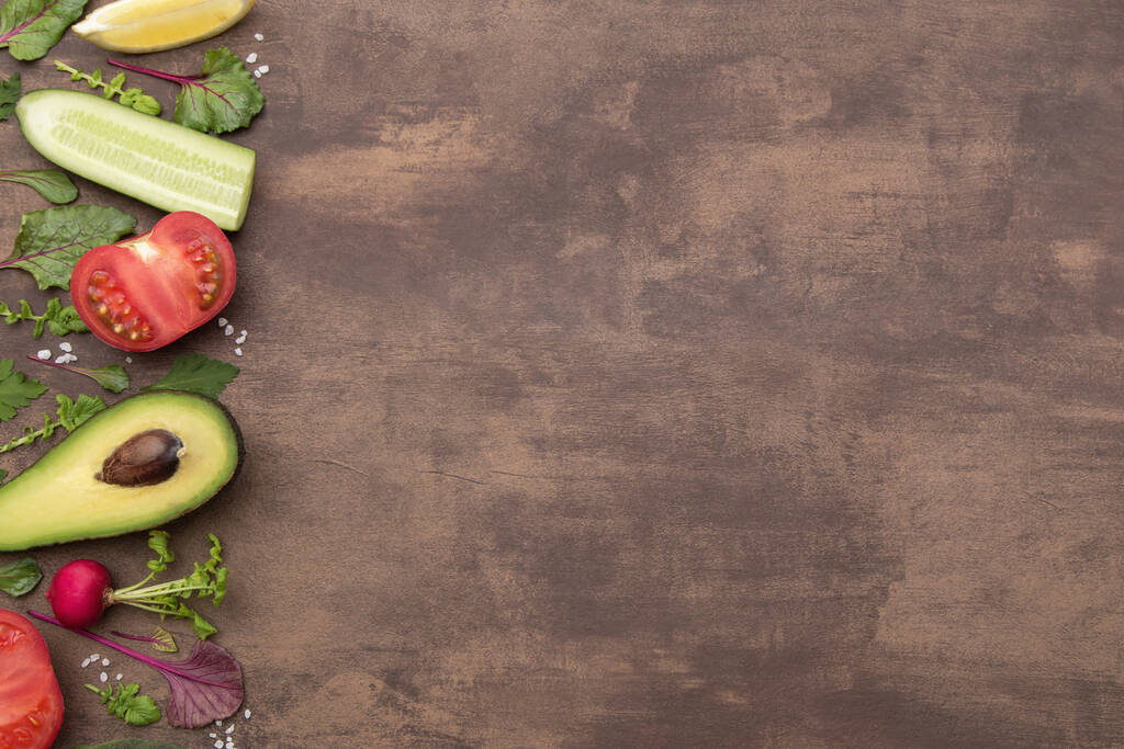 Koken achtergrond met verse groenten en kruiden. Gezond vegetarisch voedsel, dieetvoedingsingrediënten voor salade op bruine tafel, bovenaanzicht, kopieerruimte, plat leggen - Foto, afbeelding