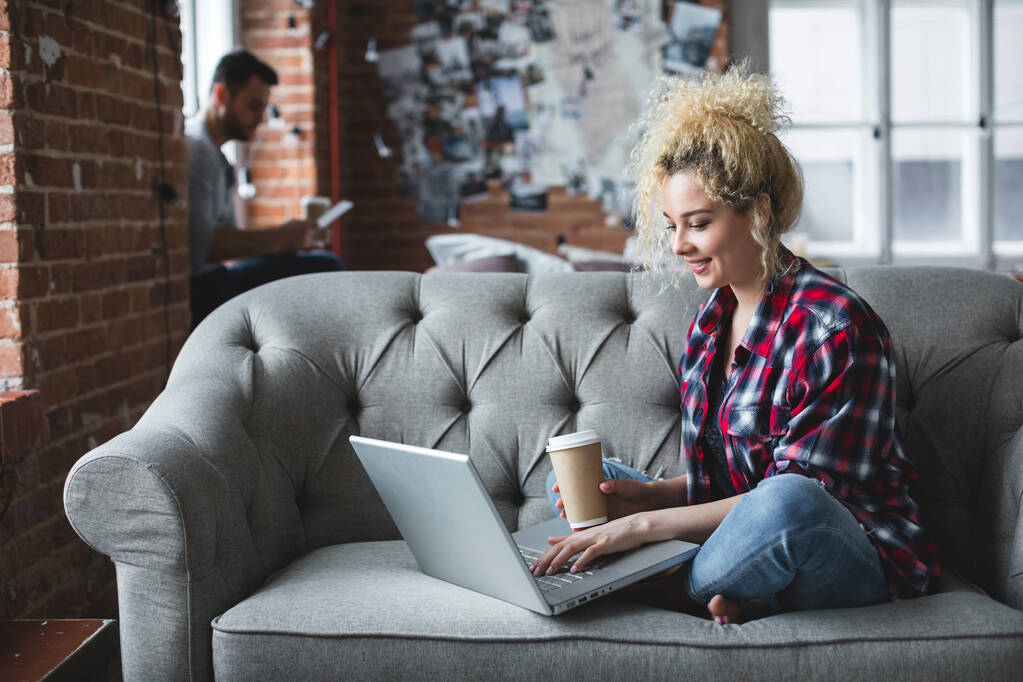 Sorrindo mulher branca bonita freelancer no sofá executa o trabalho remoto no computador portátil em casa. Vida doméstica. - Foto, Imagem