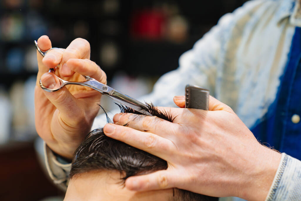 kadeřník dělá sestřih pro bruneta muže s nůžkami v holičství - Fotografie, Obrázek