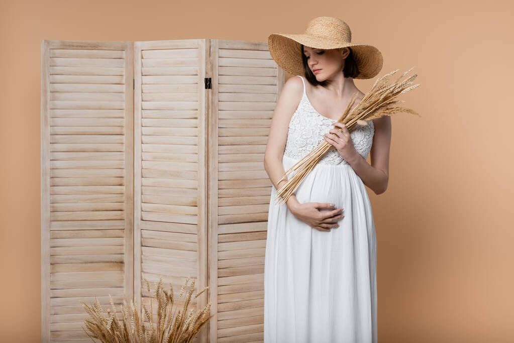 Terhes nő ruha gazdaság tüskék és megható has közelében összecsukható képernyő elszigetelt bézs  - Fotó, kép