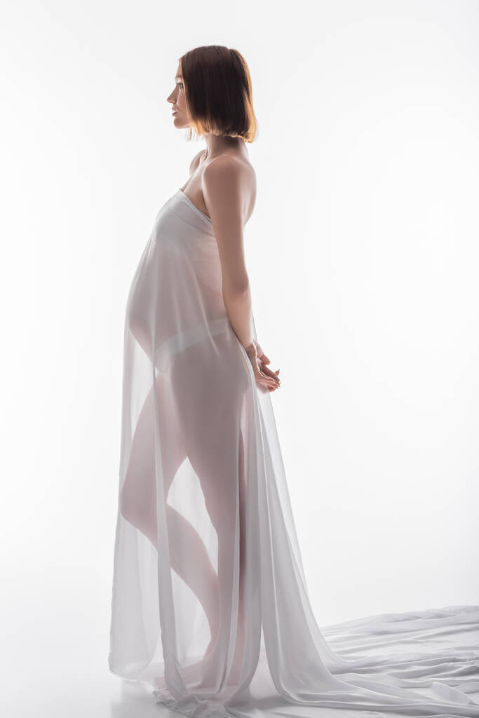 Vue latérale de la femme enceinte en tissu debout sur fond blanc  - Photo, image