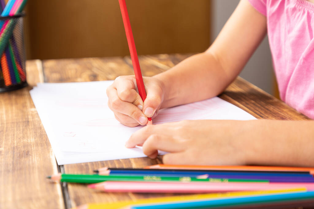 Ένα κοριτσάκι ζωγραφίζει ένα χαρτί με ένα μολύβι στο τραπέζι. - Φωτογραφία, εικόνα