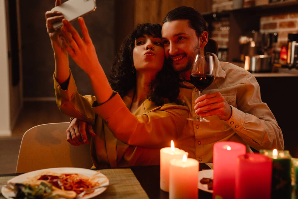 wit paar het nemen van selfie op mobiele telefoon tijdens romantische date thuis - Foto, afbeelding