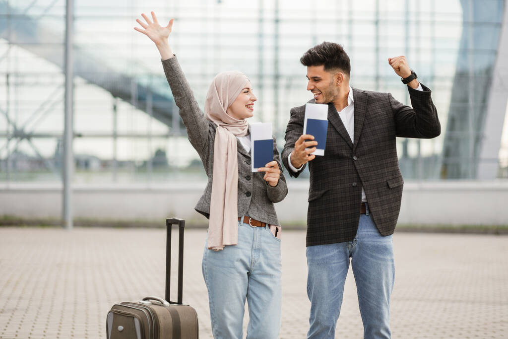 Pareja musulmana, posando en cámara afuera del aeropuerto, demostrando sus pasaportes y boletos - Foto, imagen