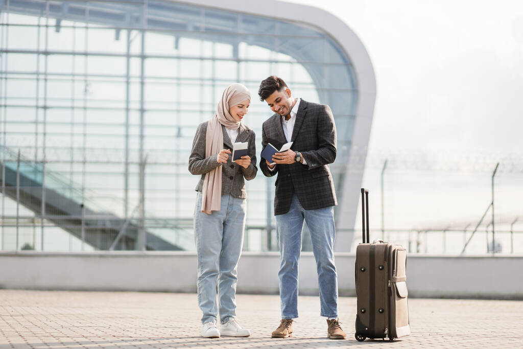 Senhora muçulmana em hijab, e homem árabe, transportando mala fora do aeroporto, segurando passaportes e bilhetes - Foto, Imagem