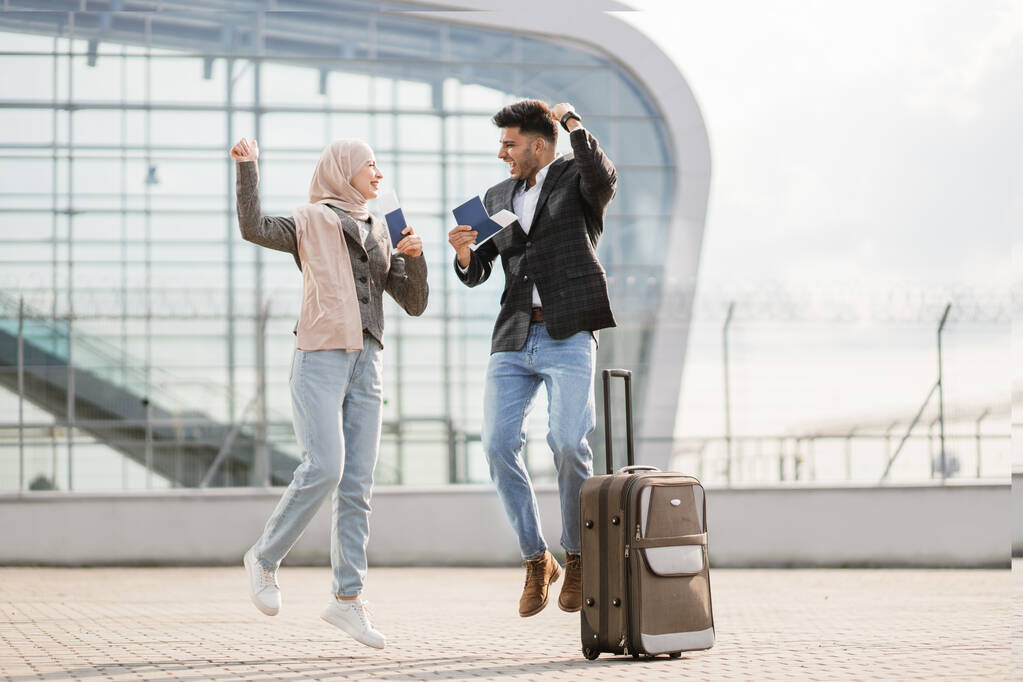 Muslim lady in hijab and Arab man, are glad and jumping together, standing outside modern airport - Photo, Image