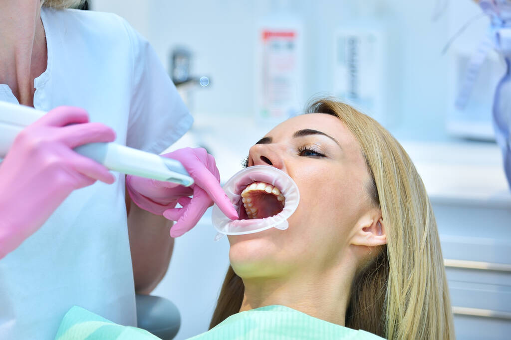 Vrouwelijke tandarts met roze handschoenen die de tanden van de patiënt schrobben met 3D-scanner. Concept voor controle en stomatologie - Foto, afbeelding